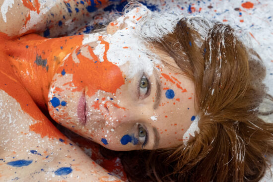 Rothaarige - im Gesicht und am Oberkörper mit Farbklecksen bespritzt.